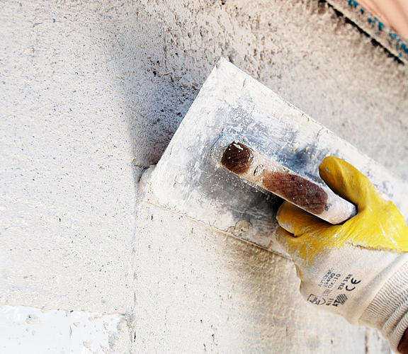 Hand mit Kelle verputzt eine Wand